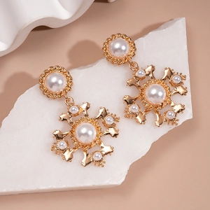 Detail of baroque pearl cross earrings with gold metallic finish on marble background