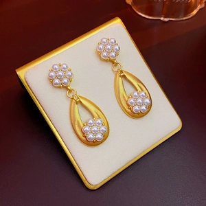 Detailed shot of golden vintage teardrop pearl earrings with floral accents on beige stand