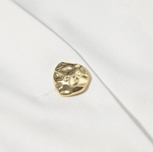 Gros plan détaillé d'un bouton en métal doré irrégulier texturé sur tissu sergé blanc