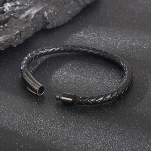 Detail of black braided leather bracelet with black magnetic clasp on textured background