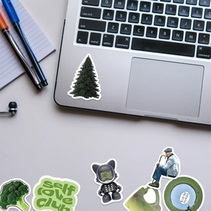 Flat lay of cute vinyl stickers featuring a Christmas tree on a laptop and stationery