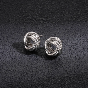 Detail view of silver knotted earrings with polished metal coils on a dark stone surface