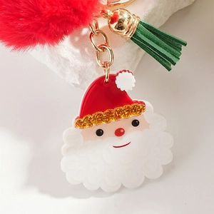 Christmas Santa Claus keychain with red fur pompom and green tassel on stone surface
