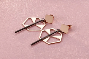 Detail of rose gold and black geometric earrings on a textured pink background