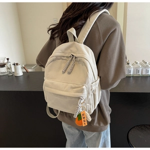 Detail of off-white corduroy backpack featuring a cute orange persimmon charm on side