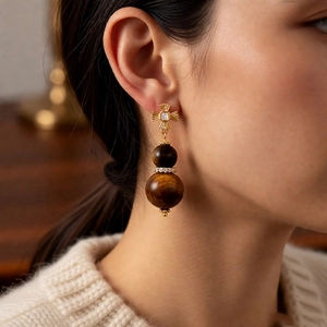 Detailed view of tiger eye gourd earrings in gold finish on a knitted sweater background