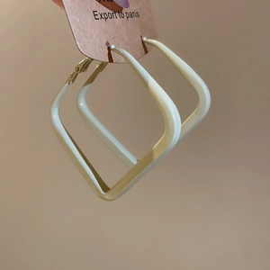 Close-up of geometric square hoop earrings in cream beige finish on a display card