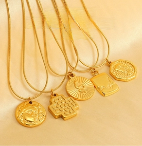 Macro detail of five gold stainless steel pendants on silk including Medusa and snake motifs