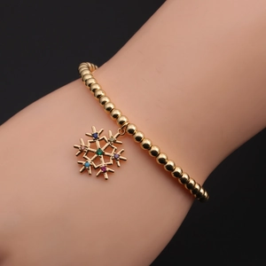 Bracelet à billes dorées avec pendentif flocon en zircons colorés porté au poignet