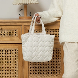 Detail of white quilted tote bag with heart pattern texture shown in a cozy home setting