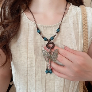 Detail of vintage butterfly pendant necklace with ceramic beads and wood ring on linen shirt