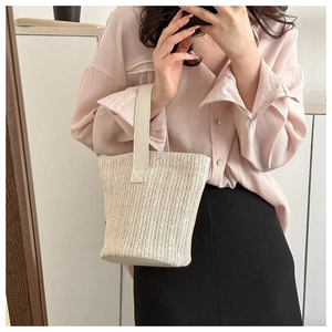 Detail of hand-woven straw texture and wide PU leather handle on a beige summer bucket bag