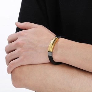 Detail of men's black rubber bracelet featuring textured gold metal bar and silver buckle