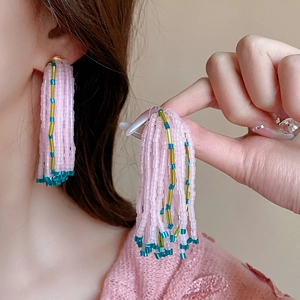 Gros plan de boucles d'oreilles à pompons roses avec accents bleus et dorés sur un mannequin