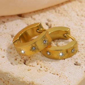 Elegant gold titanium steel hoop earrings with starburst zircon on stone background