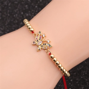 Close-up of golden butterfly bracelet with colorful zircons and adjustable red rope