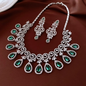 Detailed view of emerald zircon teardrop necklace and earrings set on dark brown silk fabric