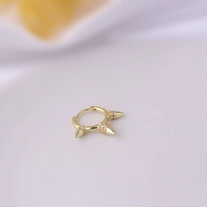 Detailed close-up of golden hoop earring with three spiked zircon studs on light background