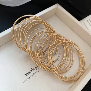 Detailed close-up of 20-piece gold bangles with diamond-cut texture on white fabric