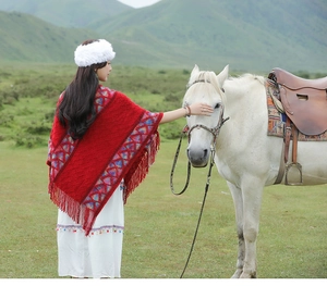 Outdoor shot of a woman in a red ethnic knit shawl with fringe interacting with a white horse