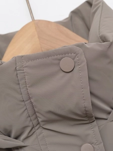 Close-up of taupe winter jacket fabric showing matte buttons and fine stitching details