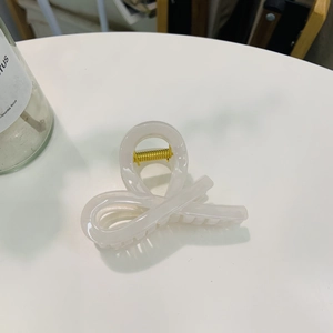 Close-up of a twisted cream white acrylic hair claw clip with golden metal spring detail
