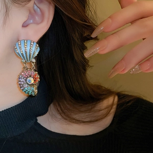 Macro shot of gold-plated shell earrings with colorful rhinestones on a female model