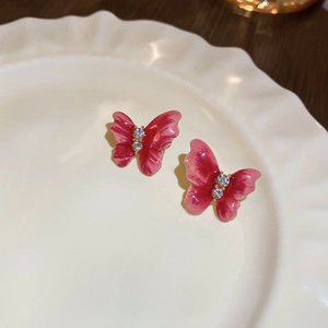 Gros plan sur boucles d'oreilles papillon émaillées rouges avec cristaux sur plat blanc