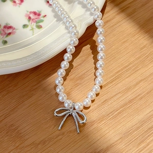 Detail view of a pearl necklace with silver bow pendant on a decorative plate