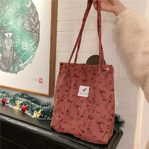 Detalle de bolso tote de pana roja con estampado de rosas, cierre de presión y asa tejida