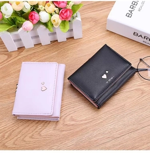 Flat lay of pink and black faux leather tri-fold wallets with metal heart on wood background