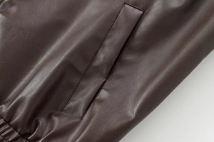 Detail of dark brown faux leather bomber jacket showing pocket seam and textured grain
