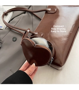 Detail of dark brown glossy leather tote bag with heart-shaped coin purse and embossed logo