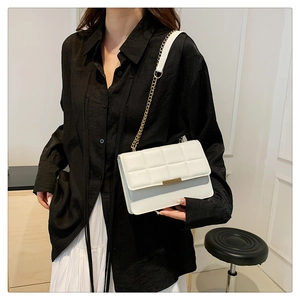 Detail of white quilted handbag featuring gold metal clasp and elegant chain strap