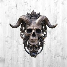 Bronze gothic skull door knocker with ornate horn details on a light wooden background