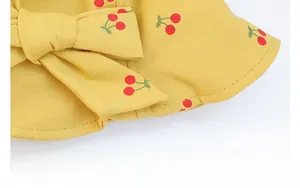Close-up of yellow baby sun hat with red cherry print and large bow detail