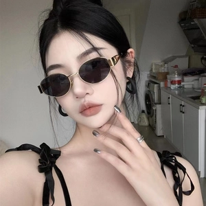 Detail of oval metal sunglasses with gold frame and dark lenses on a model