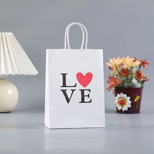 White kraft gift bag with heart LOVE print and twisted paper handles on a minimalist table