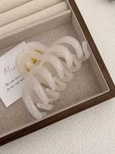 Macro detail of large cream octopus hair claw clip with golden spring in a wooden tray
