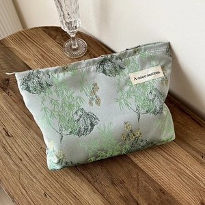 Green fabric makeup bag with bamboo print and vintage Chinese style on a wooden desk