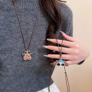 Macro detail of cartoon puppy and paw pendant necklaces on a grey knit sweater