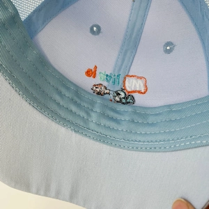 Detailed close-up of fine embroidery on light blue kids mesh trucker hat with breathable fabric
