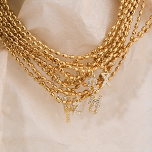 Gold beaded necklace with zircon-encrusted alphabet pendant on a textured background