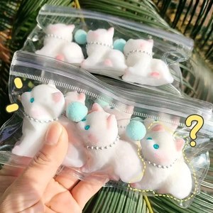 Close-up of white cat squishy toy in packaging with blue pom poms on nature background