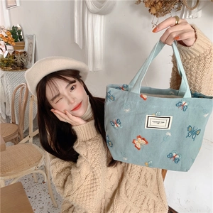 Détail d'un sac cabas en toile bleu clair avec broderie papillon et étiquette