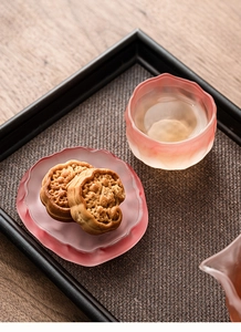 Pink frosted glass teacup with a matching saucer on a wooden table for tea ceremony