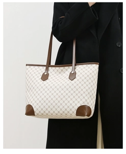 Detail of beige tote bag with chain pattern and brown leather handles on black coat