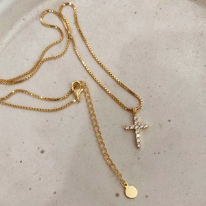 Elegant gold cross necklace with white zircon pendant on a beige ceramic plate