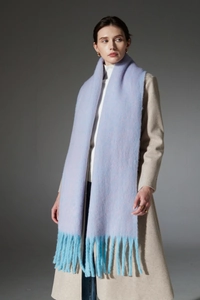 Detail of light blue bouclé yarn scarf with thick teal tassels on a stylish model