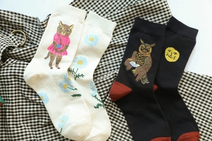 Detail of whimsical knit socks featuring cat, owl, daisy and moon patterns on plaid fabric